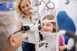 Mother and daughter talk with eye specialist when he look lens in child's eye with ophthalmoscope